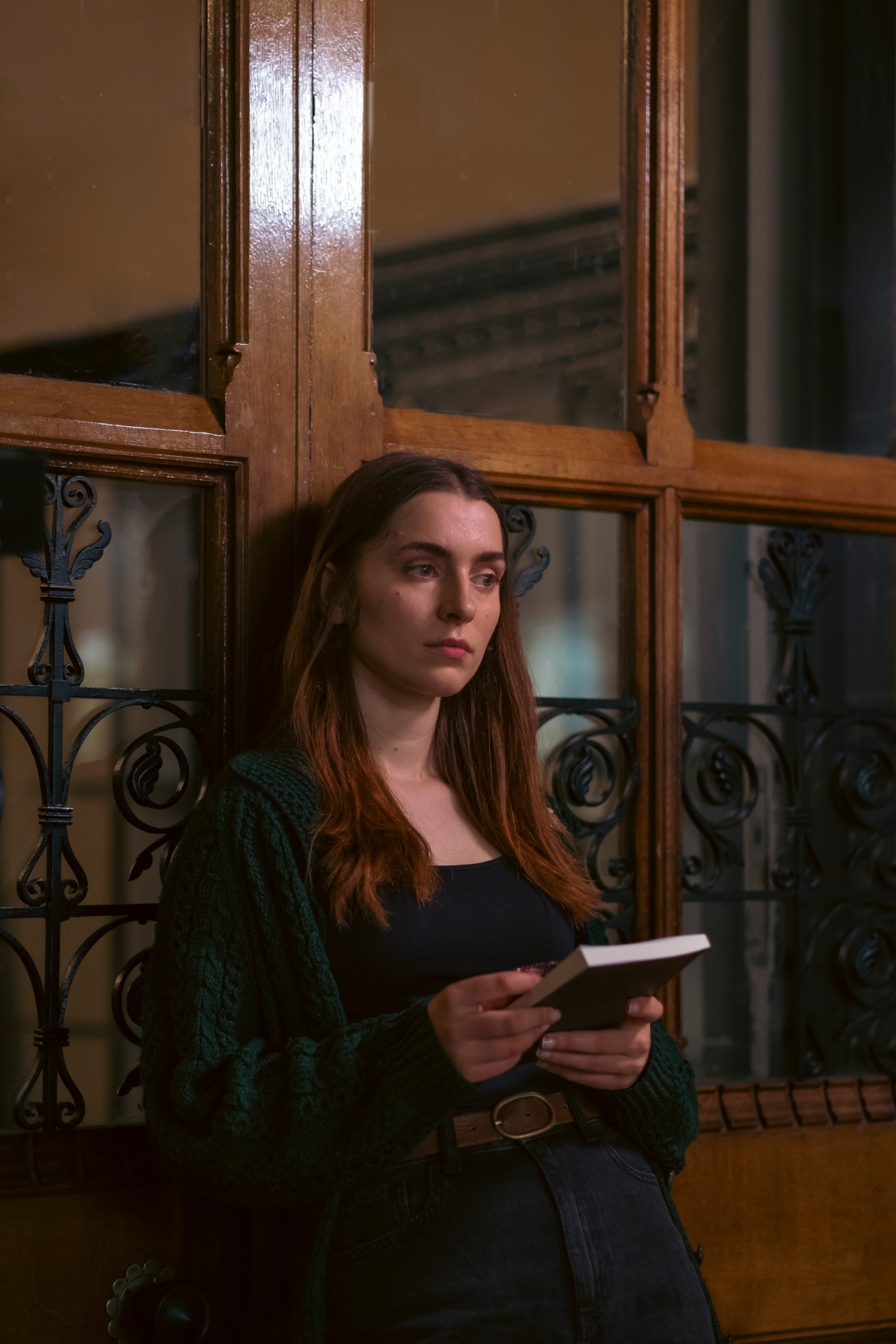 a woman leans against a door with a book in hand